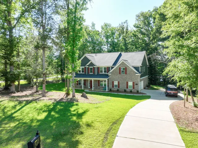 A graceful residence nestled among verdant trees, featuring a concrete driveway leading to a welcoming front entrance.