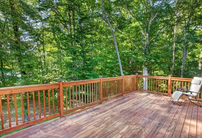 A spacious wooden deck provides a tranquil perch overlooking a verdant tree-filled landscape.
