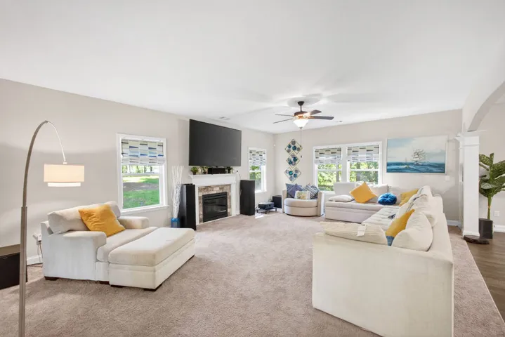A well-lit gathering space features plush carpeting, a cozy fireplace, and several windows framing verdant outdoor views.