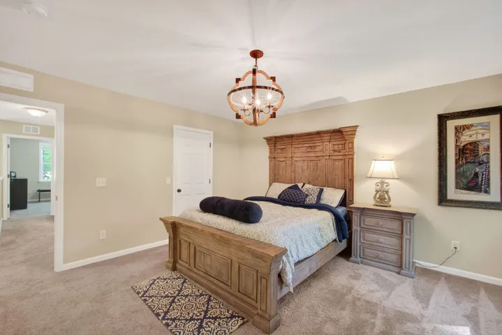 An inviting bedroom with plush carpeting features a striking wood bed frame and a charming chandelier.