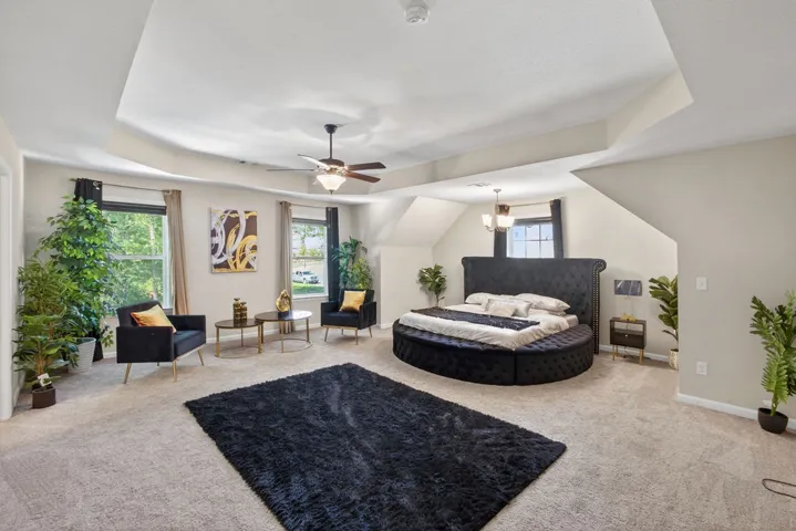 A spacious primary bedroom featuring a tray ceiling, recessed lighting, and soft carpet flooring.