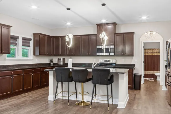 A contemporary kitchen features dark cabinetry, granite countertops, and modern pendant lighting over a breakfast bar.