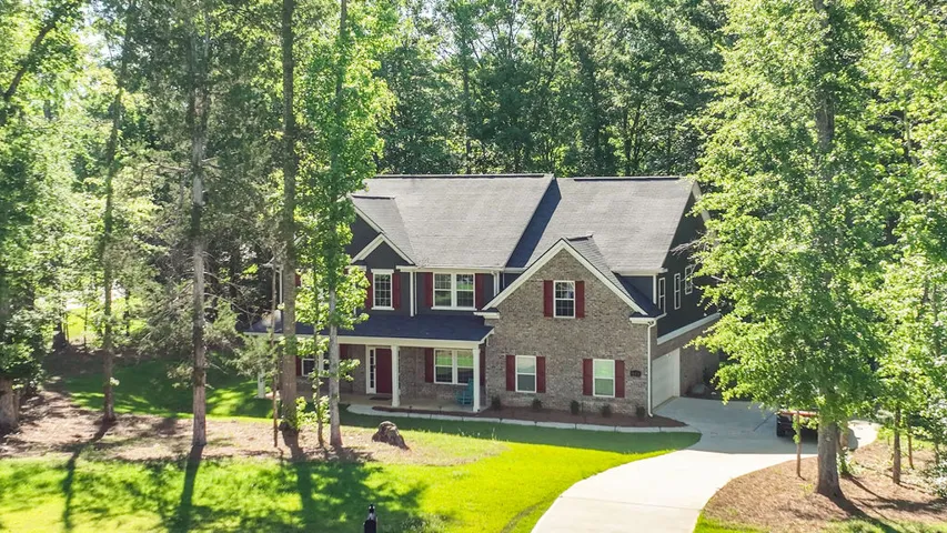 A classic brick residence nestled amidst a verdant landscape, featuring an inviting front porch and a sweeping driveway.