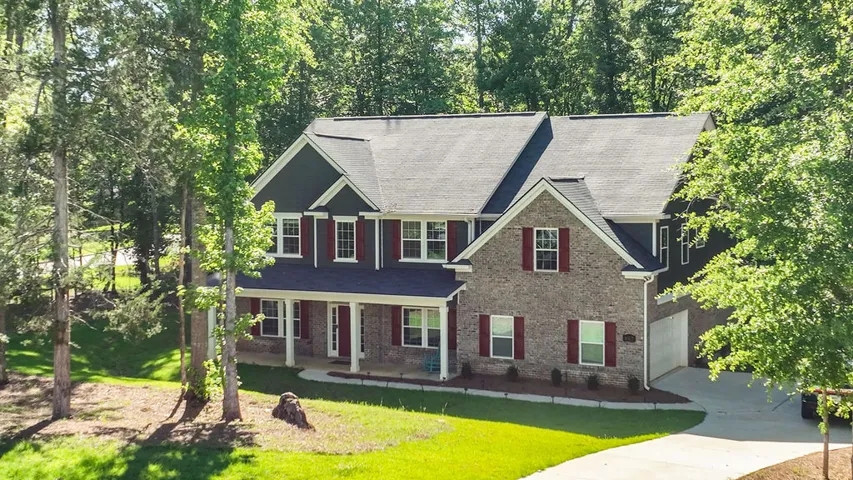 A classic brick and siding home, featuring a welcoming porch and vibrant green landscaping.