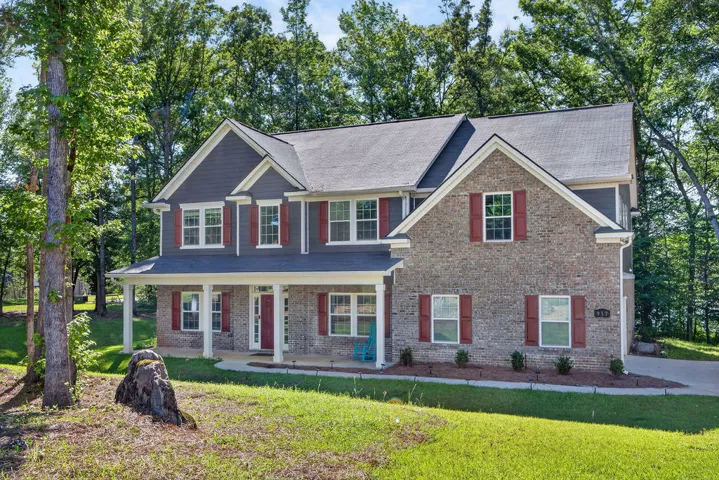 A classic brick and siding two-story home, nestled among a lush, mature tree canopy, features an inviting front porch.
