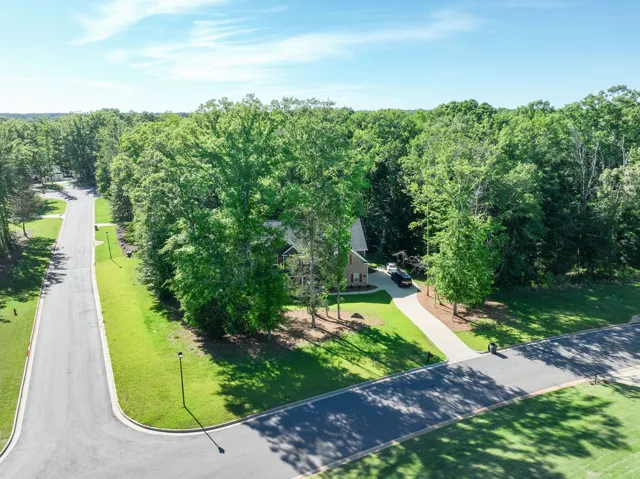 An aerial view showcases a welcoming home nestled amongst lush, mature trees, accessed via a long, paved driveway.