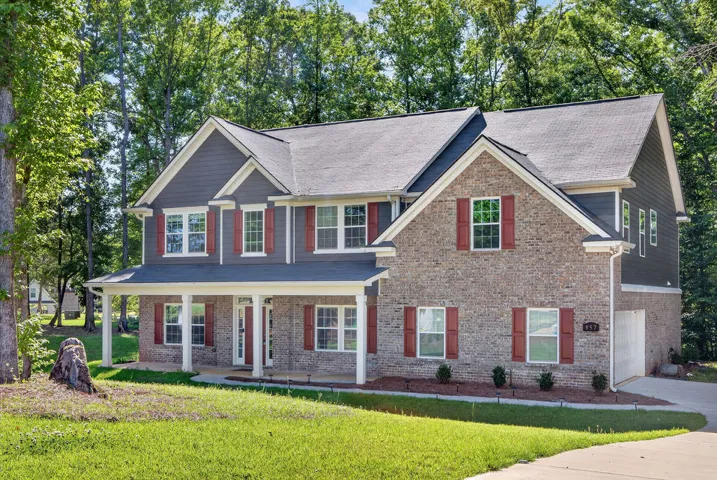 A classic brick and siding home with a welcoming covered front porch, framed by mature trees.
