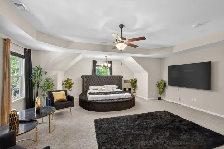 A spacious bedroom featuring sloped ceilings, a cozy carpeted floor, and ample natural light from multiple windows.