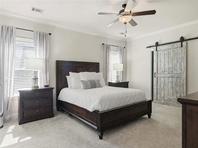A barn door paired with windows flanking the bed shapes a bright, relaxed primary bedroom.

