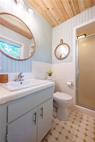 Warm wood ceiling panels contrast beautifully with light wainscoting and tiled flooring in this bathroom.
