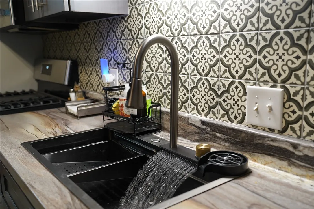 Ornate patterned tile complements the rich stone countertops surrounding a modern workstation sink.