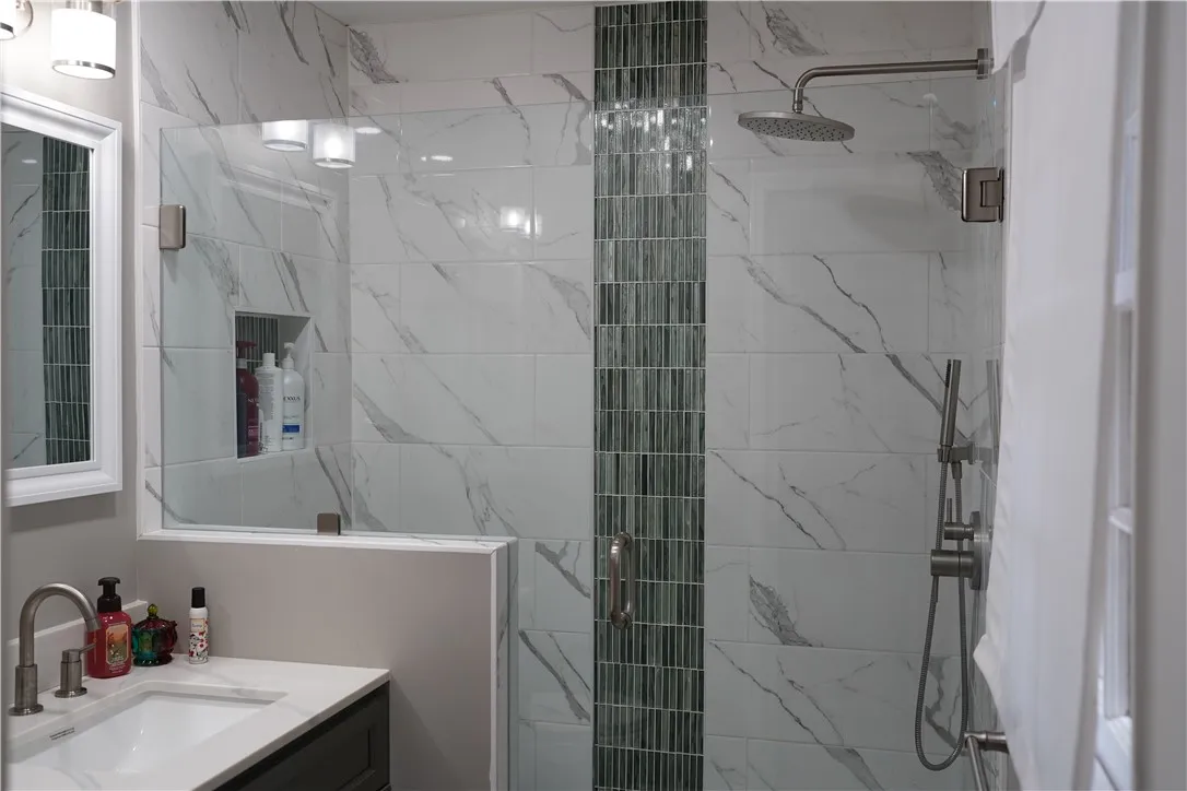 Elegantly tiled walk-in shower features a glass door alongside a modern vanity.