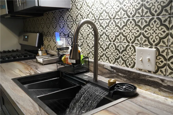 Ornate patterned tile complements the rich stone countertops surrounding a modern workstation sink.