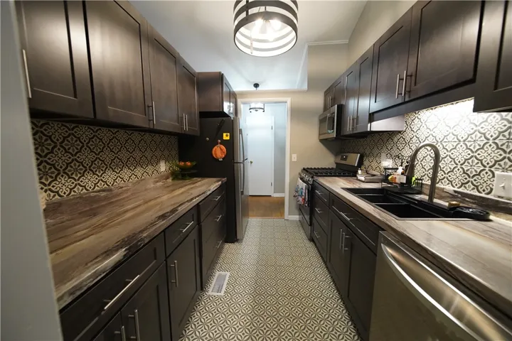 Galley kitchen featuring dark cabinetry, patterned tile flooring, and matching graphic backsplash.