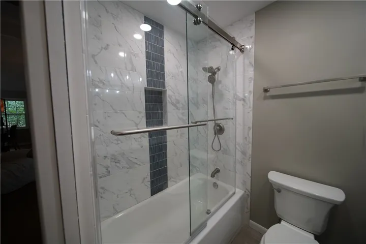 Elegant marble-patterned tile walls surround a modern bathtub behind sliding glass doors.