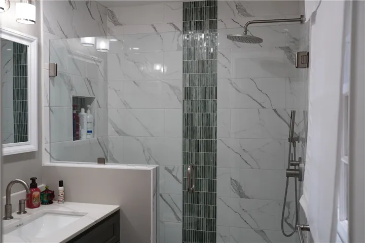 Elegantly tiled walk-in shower features a glass door alongside a modern vanity.