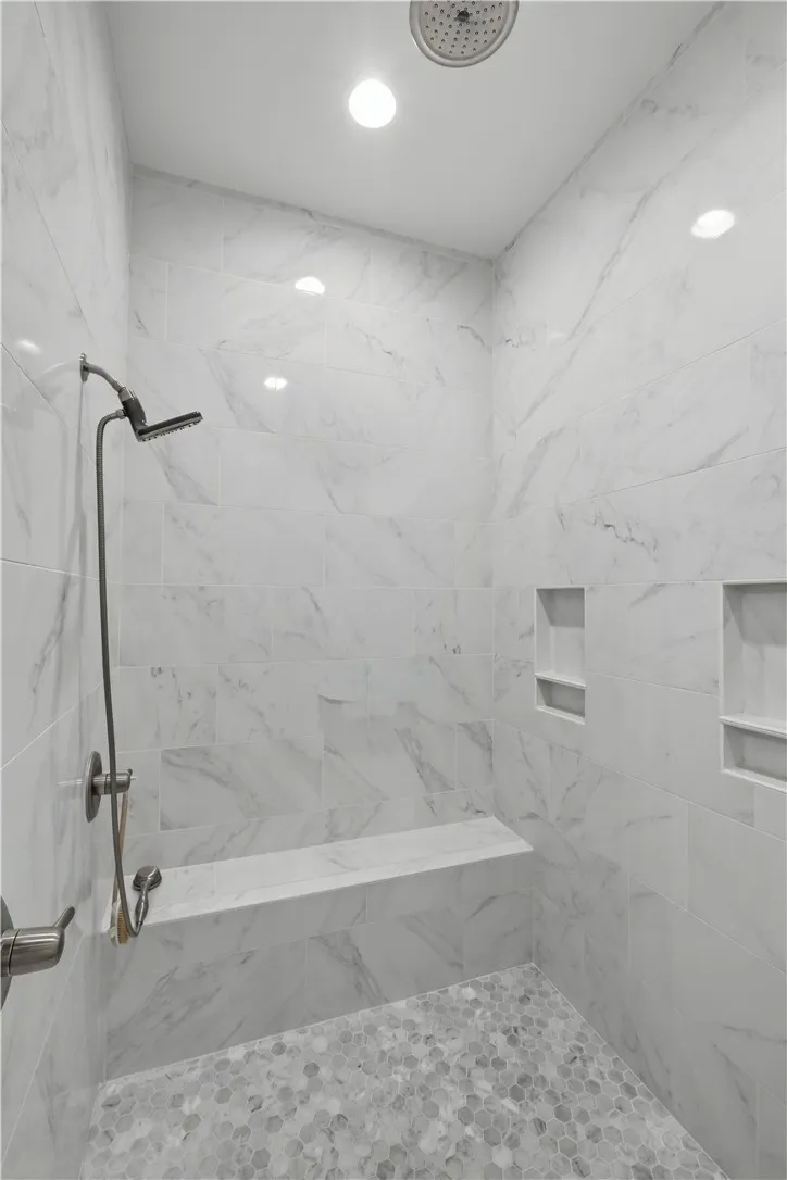 The zero-entry shower features floor-to-ceiling tile, a full-width bench, and multiple niches for toiletries.