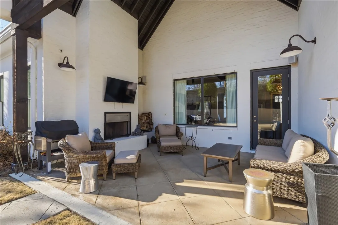 The rear porch is a well-appointed outdoor living space, featuring a vaulted ceiling, wood-burning fireplace, mounted television and speakers, built-in wood storage, and views of the pool.
