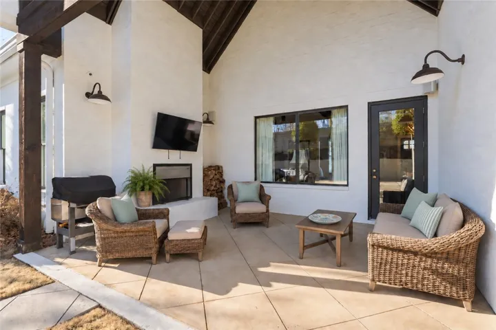 The rear porch is a well-appointed outdoor living space, featuring a vaulted ceiling, wood-burning fireplace, mounted television and speakers, built-in wood storage, and views of the pool.
