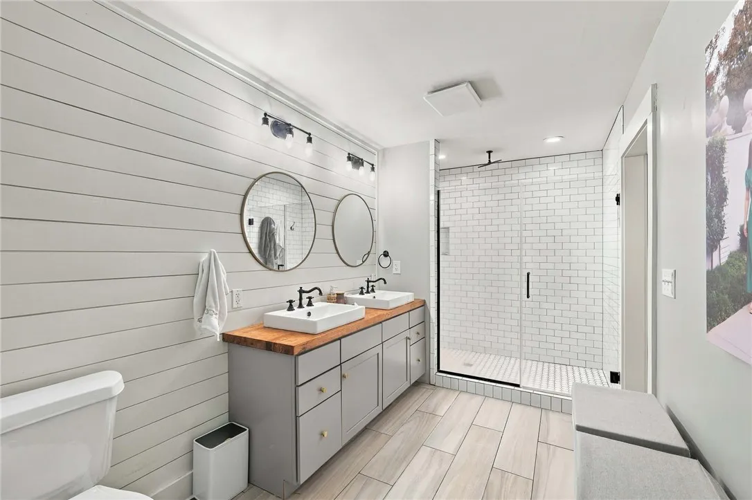 Shiplap walls and a wood-topped vanity anchor this updated bathroom with a glass shower enclosure.