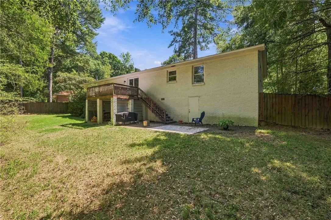 A spacious grassy lawn bordered by towering trees surrounds the home's rear exterior.