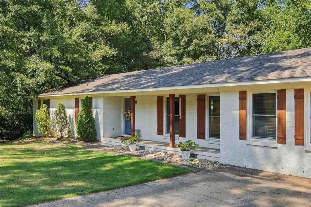 Shaded trees frame this brick ranch home featuring classic wooden shutters and a welcoming front porch.