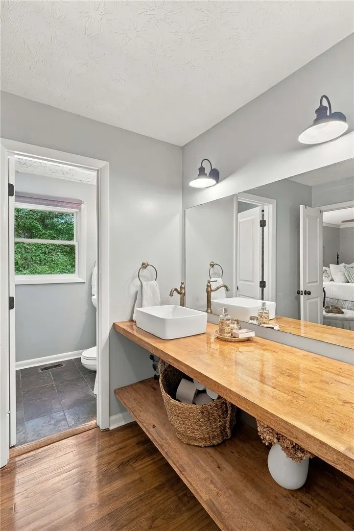 A spacious wood vanity provides warmth and ample open shelving under a large fitted mirror.