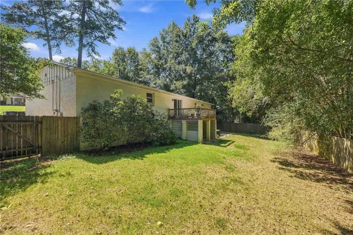 A spacious grassy lawn bordered by mature trees and wood fencing surrounds the raised deck.