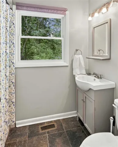 A classic bathroom featuring dark tile flooring and a window looking out to lush trees.