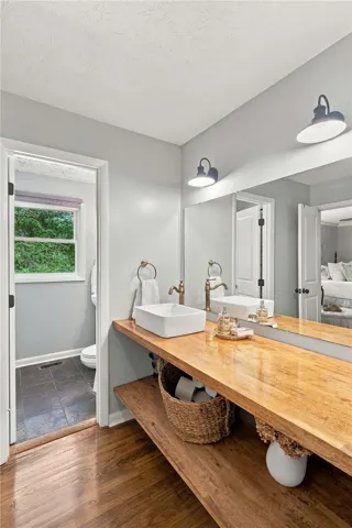 A spacious wood vanity provides warmth and ample open shelving under a large fitted mirror.