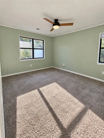 Natural light streams across the textured carpet and paneled walls of this versatile space.