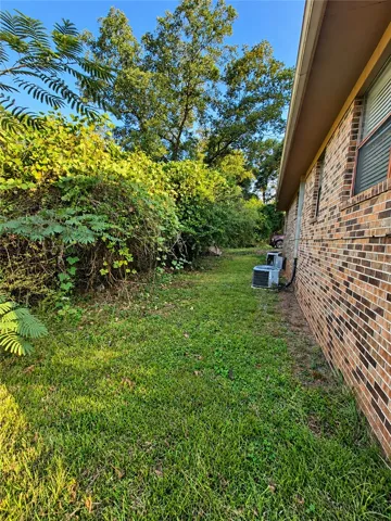 Mature trees and dense foliage border a grassy side yard running alongside the brick exterior.