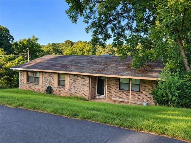 Mature trees shade a classic brick exterior situated on a gently sloping grassy lawn.