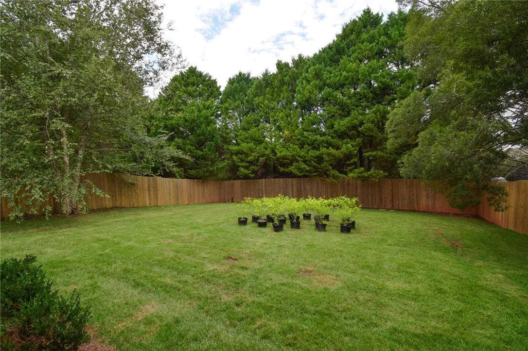 Mature trees line a spacious lawn enclosed by a wooden privacy fence.
