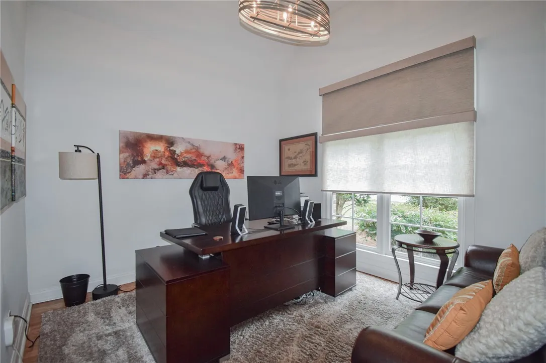 A spacious home office provides high ceilings, rich wood flooring, and a large multi-pane window.