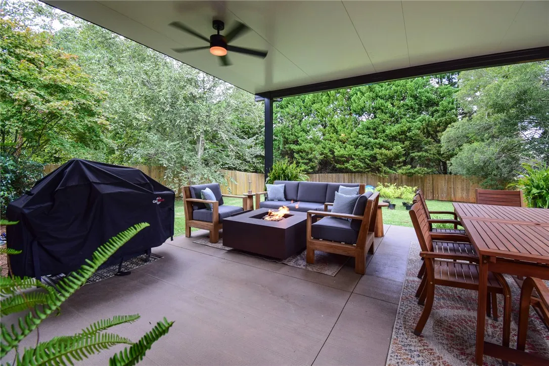 A spacious covered patio overlooks a lush lawn enclosed by a wooden privacy fence.