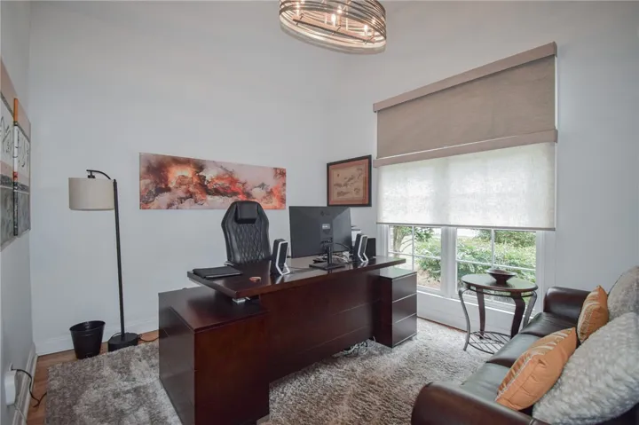 A spacious home office provides high ceilings, rich wood flooring, and a large multi-pane window.