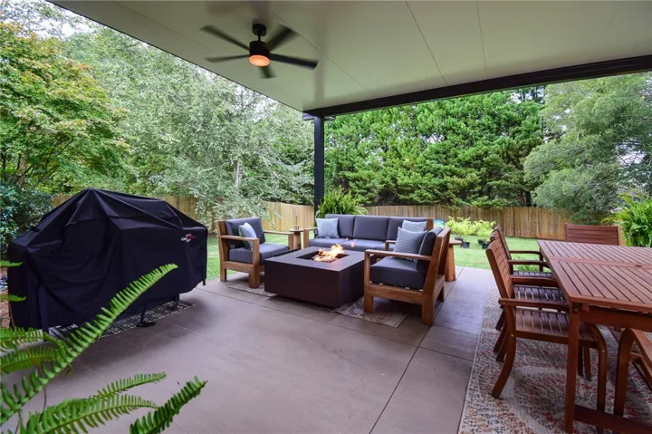 A spacious covered patio overlooks a lush lawn enclosed by a wooden privacy fence.