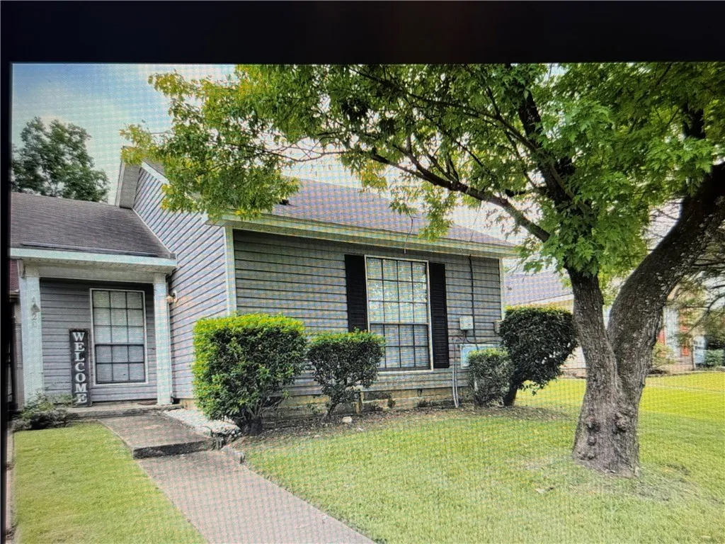 Mature trees shade the front lawn and concrete walkway leading to the entry.