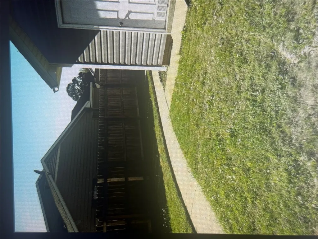A paved concrete walkway spans across the grassy backyard area enclosed by privacy fencing.