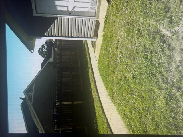 A paved concrete walkway spans across the grassy backyard area enclosed by privacy fencing.