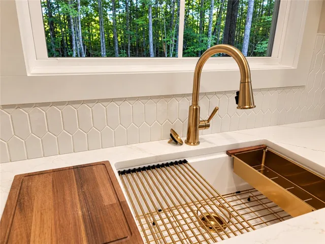 An elegant kitchen sink area features premium stone counters and a picture window overlooking forest views.