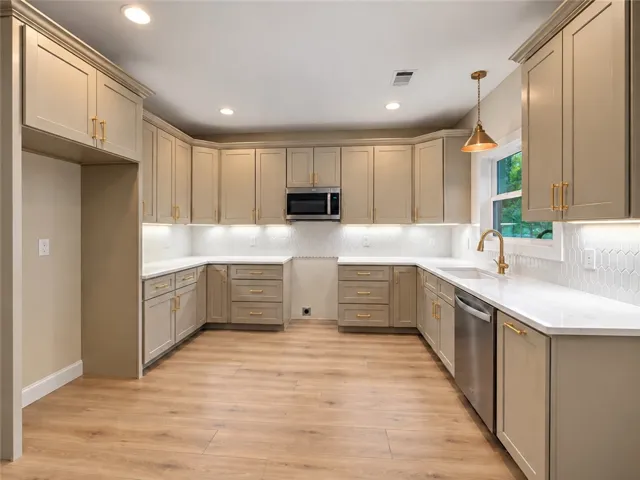Warm wood flooring grounds this modern culinary space featuring abundant cabinetry and clean countertops.