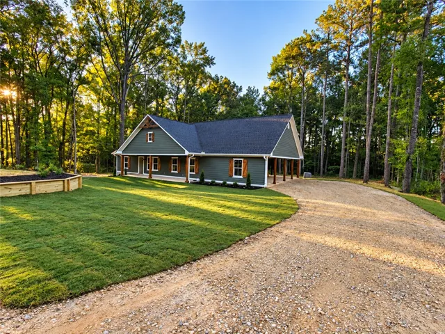 Towering trees frame a gravel driveway leading to this craftsman home with custom board shutters.
