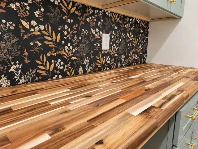 Rich butcher block countertops pair beautifully with a bold botanical pattern backsplash.