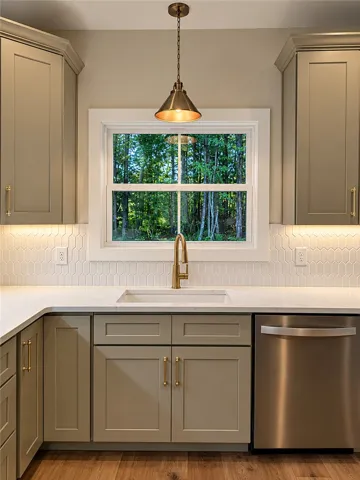 A classic kitchen sink station overlooks lush backyard woods through a bright window.