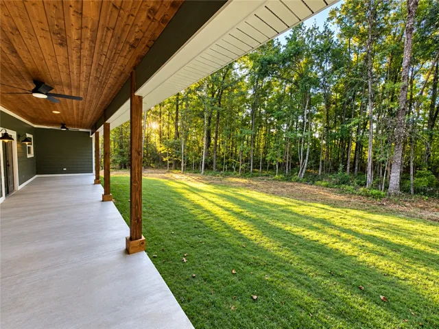A spacious covered back porch features a warm wood ceiling and overlooks a lush, wooded lawn.