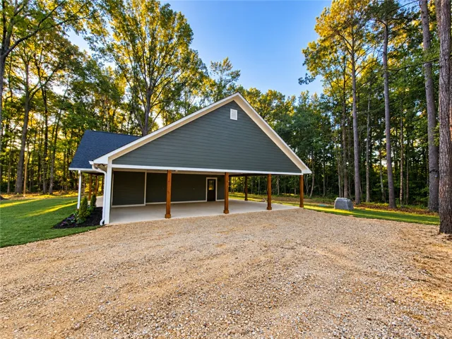A spacious covered carport stands framed by towering trees in a serene wooded setting.