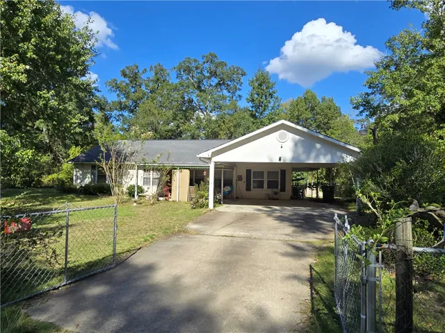A spacious concrete driveway leads past gated chain-link fencing directly to the attached carport.