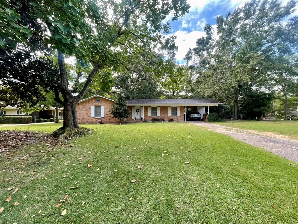 Mature trees shade a classic brick ranch home nestled on a grassy lawn.